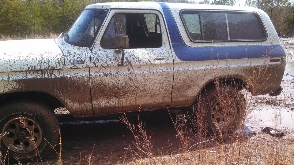 Mud-covered white and blue 1978 Ford Bronco side view, stuck in mud