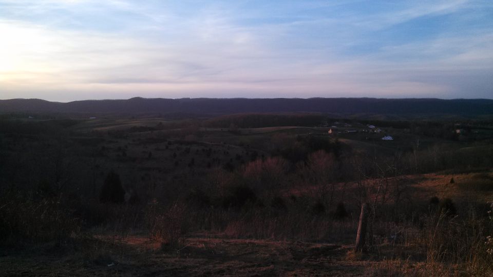 rolling hills and sky at dusk with a small cluster of buildings in the distance