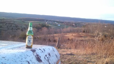 1979 Ford Bronco - A bottle of Yuengling Lager sits on a vehicle part with a view of the countryside.
