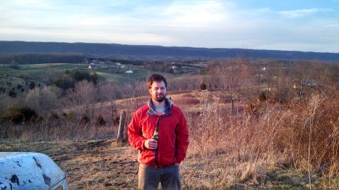 1979 Ford Bronco - A man stands in a field with a beer, overlooking a valley under a cloudy sky.