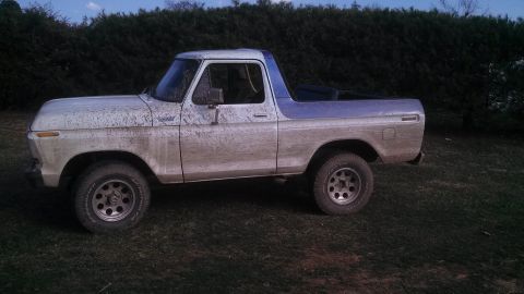 1979 Ford Bronco - This muddy Ford Bronco is parked on grass in front of a hedge. The vehicle has a two-tone paint scheme.