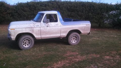 1979 Ford Bronco - A dirty 1978 Ford Bronco is parked on a grassy area with a hedge in the background.