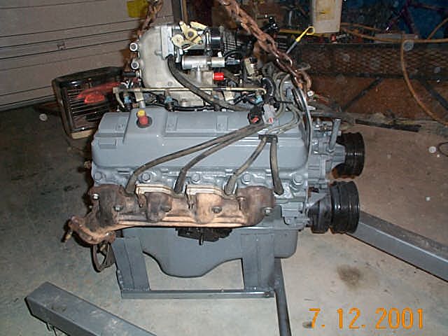 Gray inline engine on a stand with rusty exhaust manifold in a garage