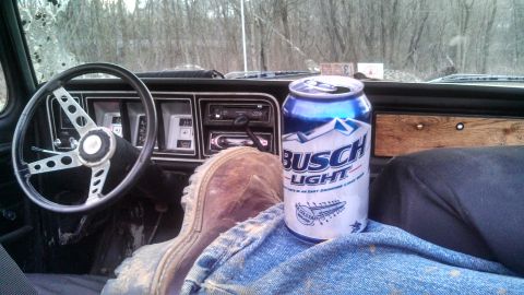 1979 Ford Bronco - A can of Busch Light sits on the seat inside a truck cab, next to the driver's boot.