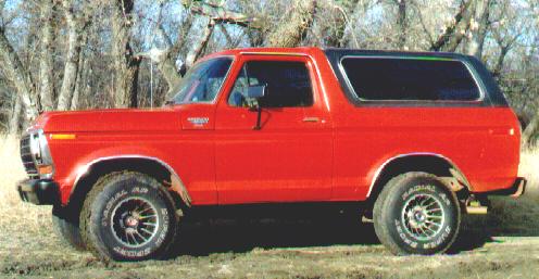Red Ford Bronco SUV with white top, side view, parked on grass