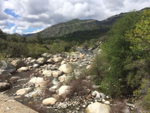 1996 Ford C-350 (Centurion Conversions) - A scenic view of a river winding through a boulder-strewn canyon, with lush green hills under a dramatic cloudy sky.