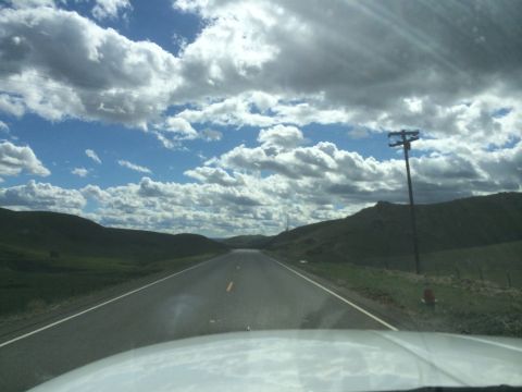 1996 Ford C-350 (Centurion Conversions) - View from a vehicle traveling on a highway through a rural landscape with rolling hills and dramatic clouds.