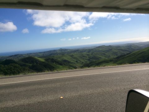 1996 Ford C-350 (Centurion Conversions) - A scenic view of rolling green hills meeting the ocean, seen from a roadside perspective.