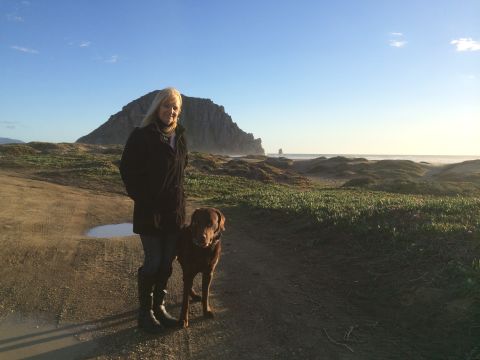 1996 Ford C-350 (Centurion Conversions) - A woman and her dog pose for a photo on a coastal path with a prominent rock formation in the distance.