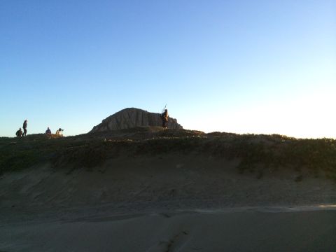 1996 Ford C-350 (Centurion Conversions) - A group of people are gathered on a sandy hill near a prominent rock formation at sunset.