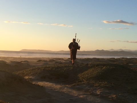 1996 Ford C-350 (Centurion Conversions) - A lone bagpiper plays on a dune-covered beach as the sun sets over the ocean.