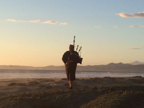 1996 Ford C-350 (Centurion Conversions) - A lone bagpiper plays on a dune-covered beach as the sun sets over the ocean.