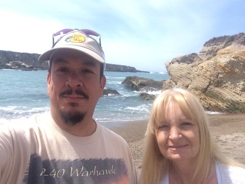 1996 Ford C-350 (Centurion Conversions) - A couple enjoys a day at the beach, with waves crashing against the rocky shore under a bright sky.