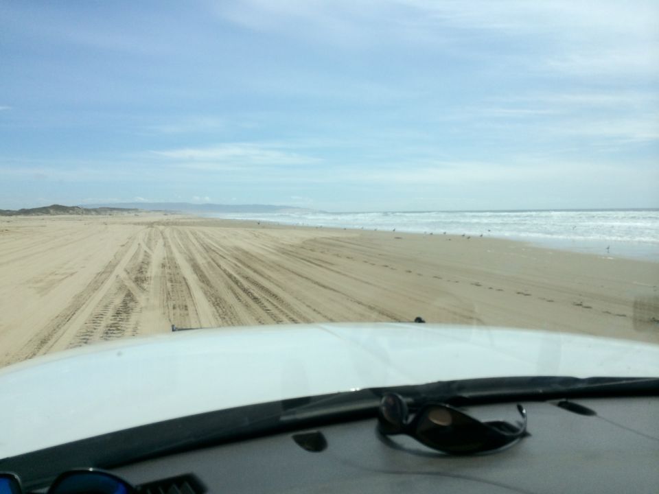 View from inside a vehicle driving on a sandy beach with the ocean in the background