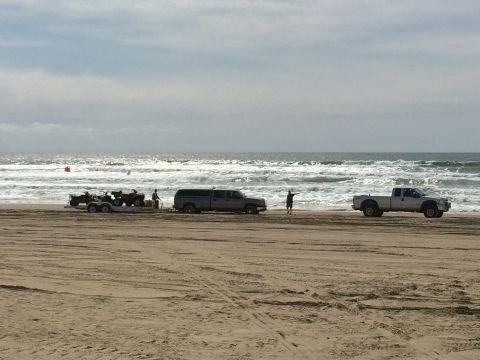 1996 Ford C-350 (Centurion Conversions) - Two pickup trucks and a trailer with ATVs are parked on a sandy beach near the ocean waves.