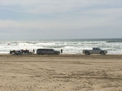 1996 Ford C-350 (Centurion Conversions) - Pickup trucks and ATVs on the beach with waves in the background.