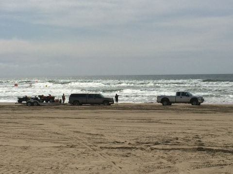 1996 Ford C-350 (Centurion Conversions) - Vehicles and ATVs parked on the sand near the ocean waves under a cloudy sky.