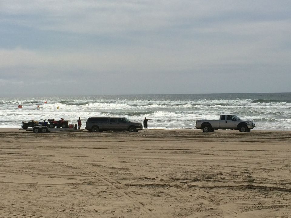 Two trucks and ATVs on a sandy beach with waves in the background
