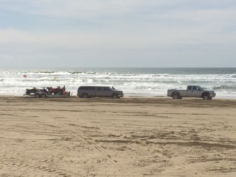 1996 Ford C-350 (Centurion Conversions) - Two pickup trucks and a trailer carrying ATVs are parked on a sandy beach near the ocean.