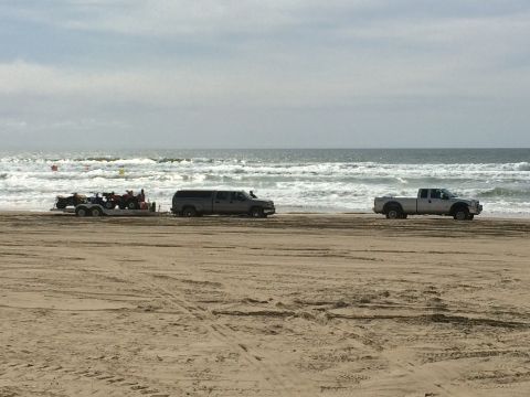 1996 Ford C-350 (Centurion Conversions) - Two pickup trucks and a trailer carrying ATVs are parked on a sandy beach near the ocean waves.