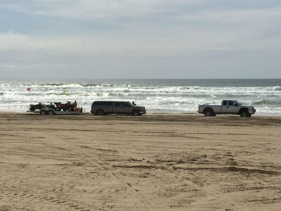 Side view of two pickup trucks and a trailer with ATVs on a beach