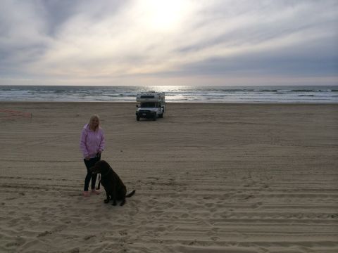 1996 Ford C-350 (Centurion Conversions) - A woman and her dog stand on a beach next to a truck camper under a cloudy sky.