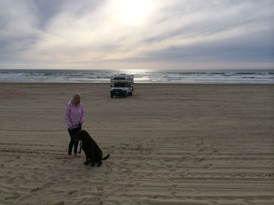White truck camper parked on a sandy beach with ocean waves in the background