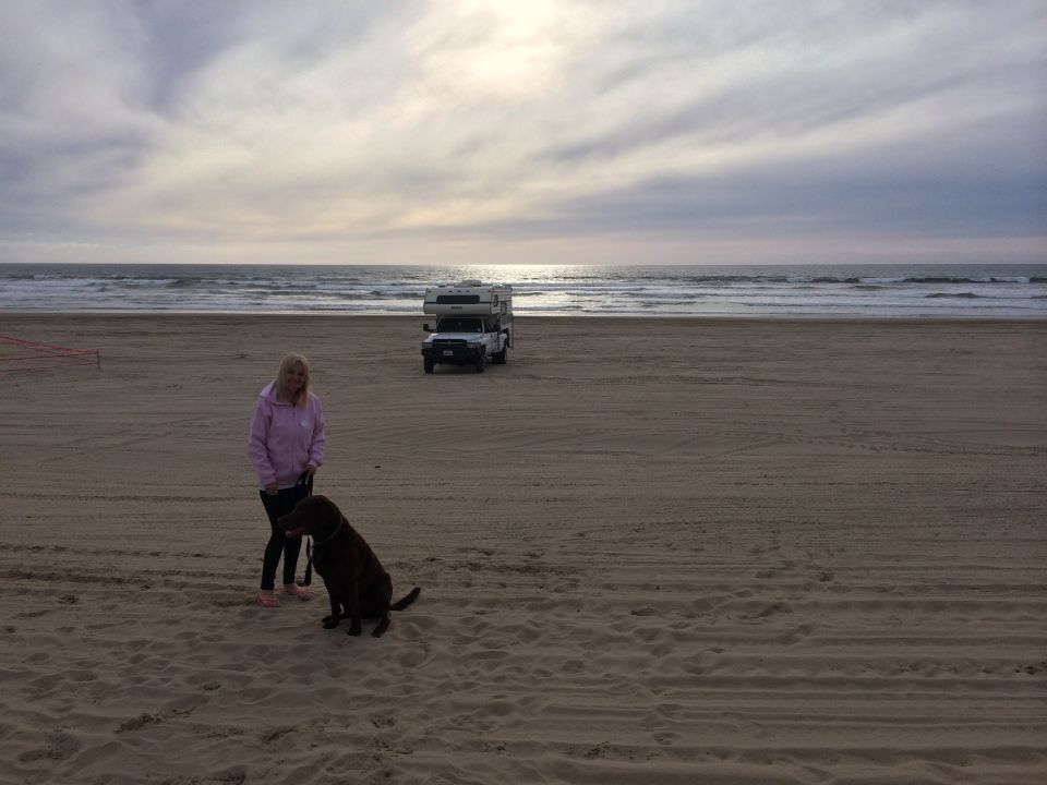 Woman with dog on sandy beach, truck camper parked near ocean