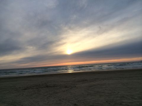 1996 Ford C-350 (Centurion Conversions) - Sunset over the ocean with waves crashing on the shore and tire tracks in the sand.