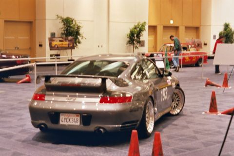 1992 Mercury Grand Marquis - A gray Porsche 911 GT2 is displayed indoors, with other vehicles and an auto show setup visible in the background.
