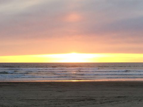 1996 Ford C-350 (Centurion Conversions) - A tranquil beach scene unfolds as the sun dips below the horizon, painting the sky with hues of orange and pink.