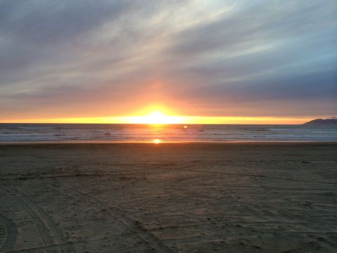 1996 Ford C-350 (Centurion Conversions) - Sunset over the ocean viewed from a sandy beach with tire tracks.