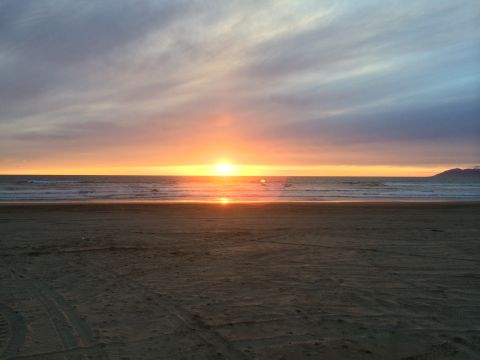 1996 Ford C-350 (Centurion Conversions) - The sun sets over the ocean, casting an orange glow across the sky and water.