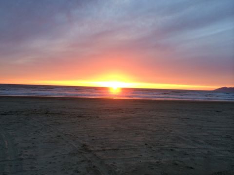1996 Ford C-350 (Centurion Conversions) - Sunset over the ocean viewed from a sandy beach with tire tracks.