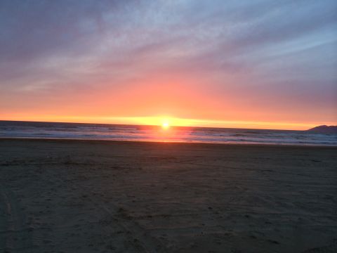 1996 Ford C-350 (Centurion Conversions) - A vibrant sunset paints the sky with orange and purple hues over the ocean and sandy beach.