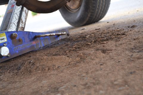 1981 Ford F-250 - A blue car jack is positioned under a tire on a dirt surface.