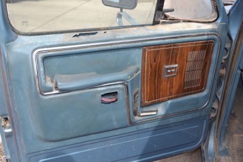 1981 Ford F-250 - Close-up of a worn blue truck door panel faux wood trim and a missing interior door handle.