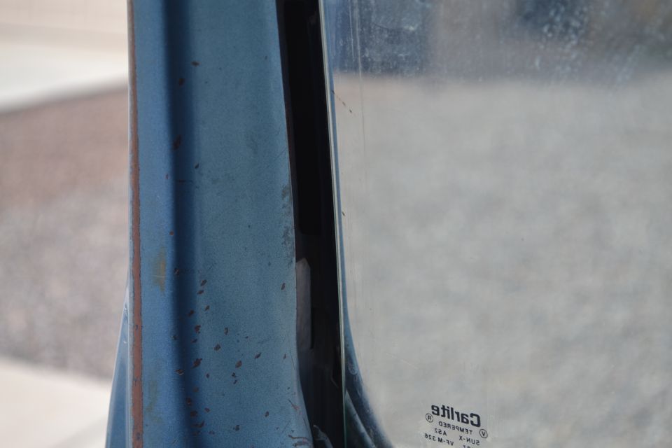 Blue painted metal door frame with rust spots next to a glass window showing a "Supermotors.net" watermark