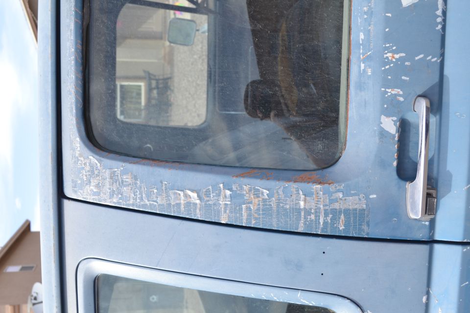 Close-up of a blue truck door with peeling paint and a chrome handle