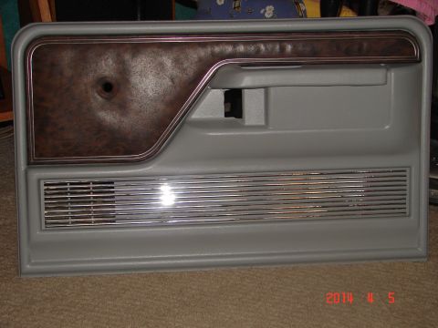1978 Ford Bronco - This gray door panel features a wood grain insert and a horizontal chrome speaker grille, likely from an older truck or SUV.