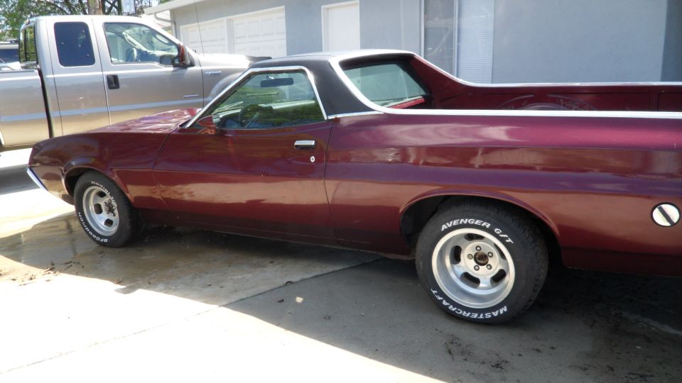 Maroon 1972 Ford Ranchero with a black vinyl top, parked next to a silver pickup truck
