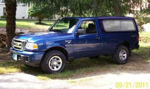 1994 Ford Bronco - This blue Ford Ranger pickup truck features a camper shell and is parked outdoors on a grassy area.