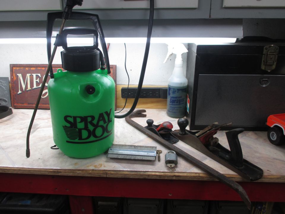 Workbench with green sprayer, crowbar, hand planes, lock, and spray bottle