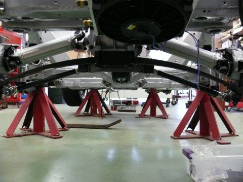 Car underbody with drivetrain components visible, supported by red jack stands