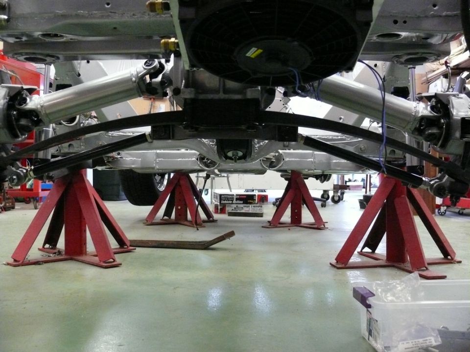 Car underbody with drivetrain components visible, supported by red jack stands