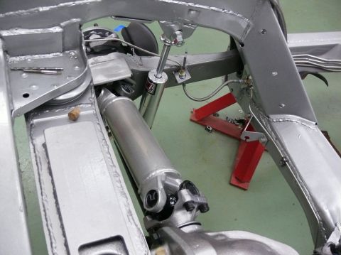 Close-up of a vehicle's silver-painted frame, driveshaft, and shock absorber