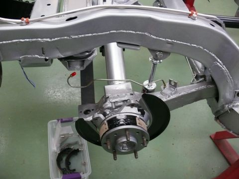 close-up of car frame, suspension, and brake assembly with parts in a bin