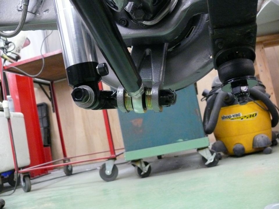 Close-up of a car's rear suspension with a shock absorber and linkage. Shop-Vac visible in background