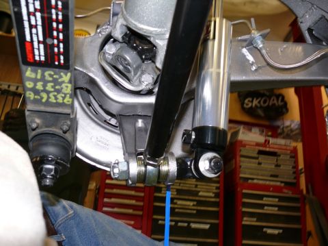 Close-up of rear suspension parts, including a shock absorber and linkage. A label with text is visible on a b