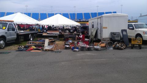 1973 Chevrolet Camaro - Various automotive parts are laid out for sale at an outdoor market with tents and stadium seating in the background.